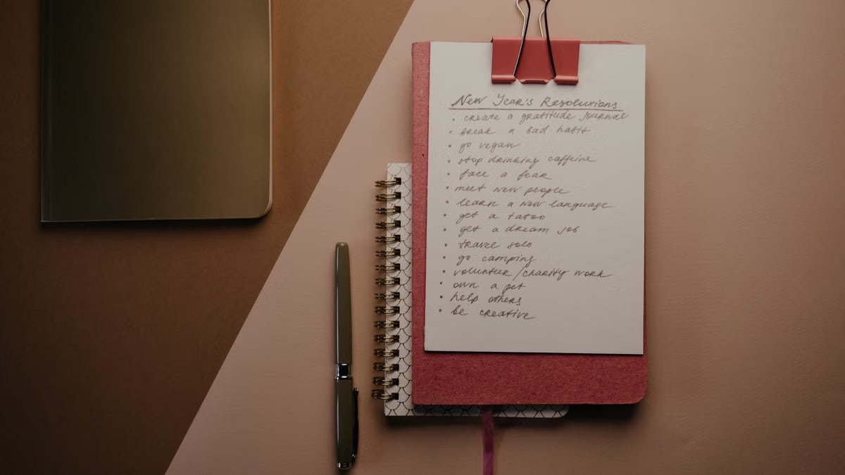 Top view of a cozy pink notebook with New Year resolutions, pen, and stylish paperclip setup.